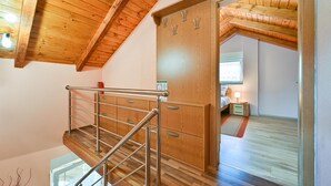 Una escalera de madera con barandillas de metal que conduce a un dormitorio con cama, mesita de noche y ventana.