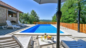Una piscina con sillones de descanso, una mesa con bebidas y fruta, y vistas al campo.