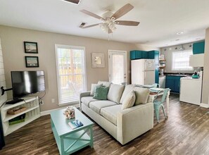 Cozy living space with a sofa, armchair, and TV, featuring a kitchenette with a refrigerator, sink, and kettle.