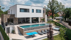 Et moderne hus med to etager, en swimmingpool, udendørs møbler og en patio.
