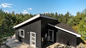 Une petite cabane en bois sombre, avec un toit en pente, une porte d’entrée et une fenêtre.
