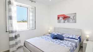 Un dormitorio con cama, ventana con cortinas, una obra de arte en la pared y lámparas de noche.
