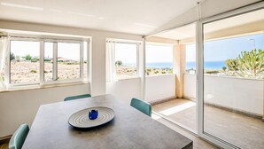 Un comedor moderno con una mesa y sillas, ventanas amplias con vistas a un paisaje desértico y al océano.
