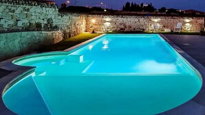 Una piscina rectangular con una pared de piedra en un lado y una zona verde en el otro.