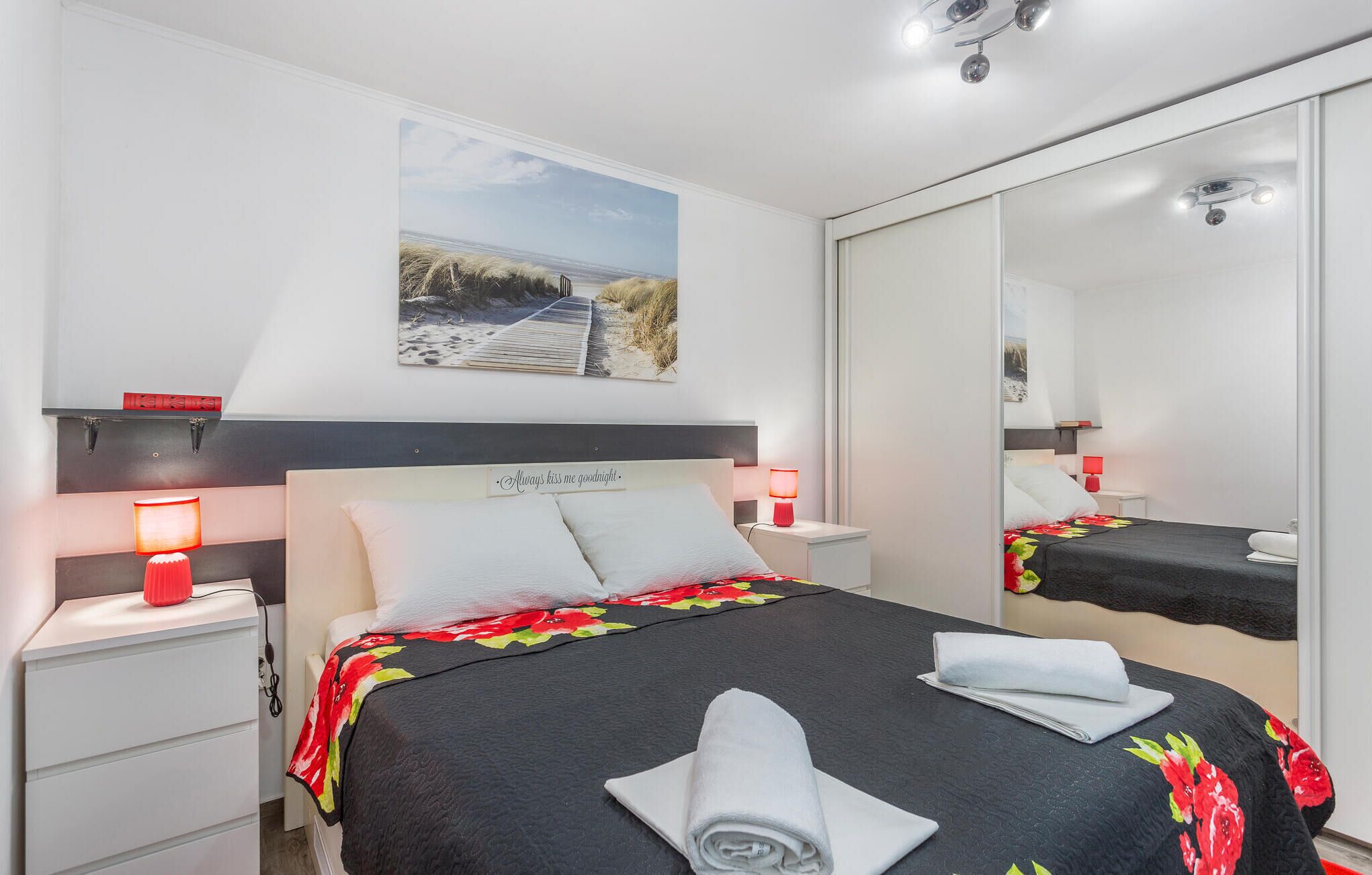 Ein modernes Schlafzimmer mit Bett, Nachttischen, einem Spiegel und einem Wandbild.