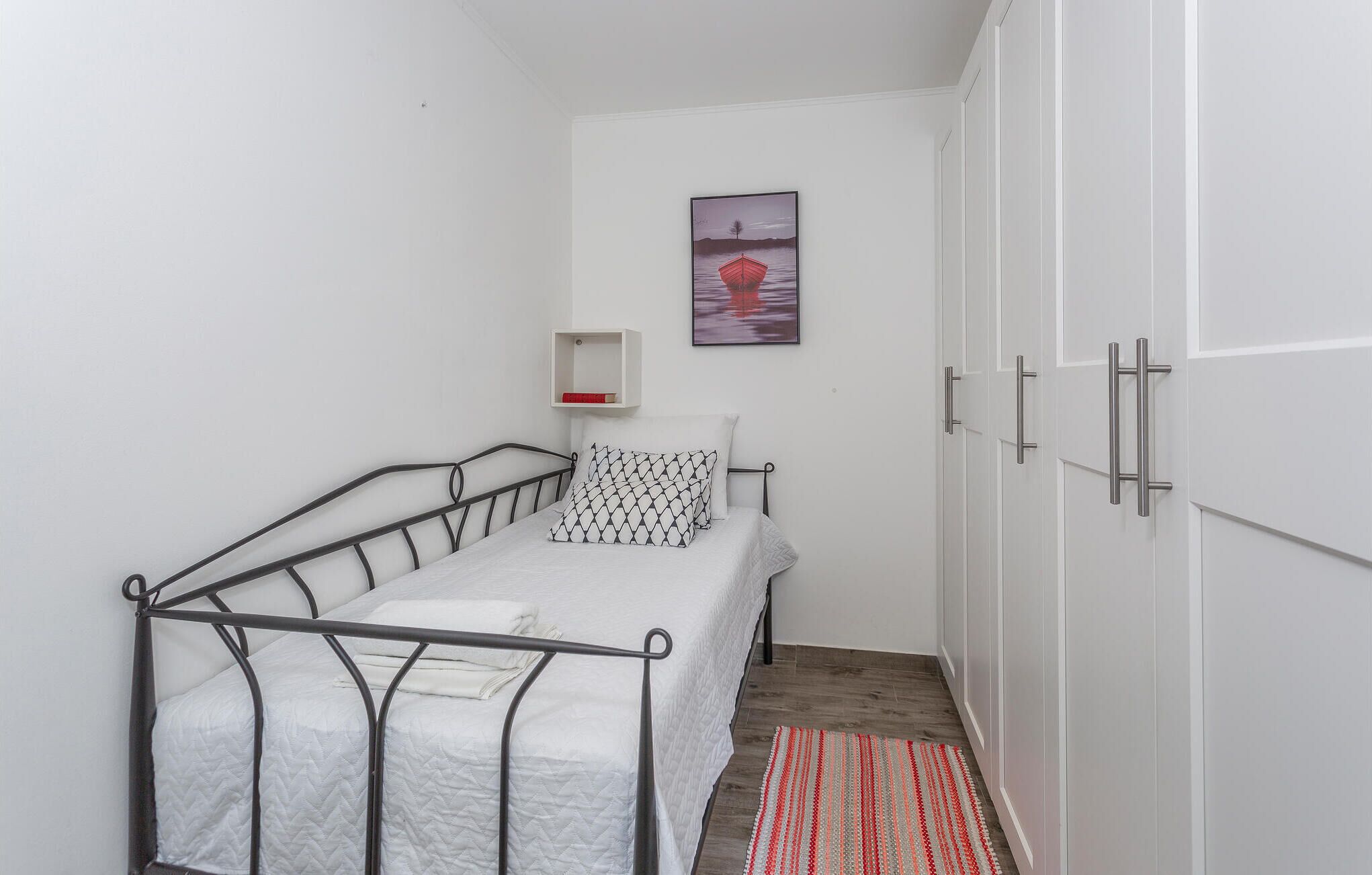 A small, well-lit room with a single bed, a wardrobe, and a framed picture on the wall.