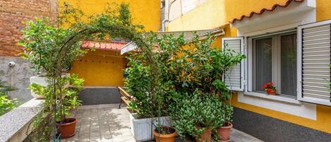 A courtyard with potted plants, a bench, and a window with shutters.