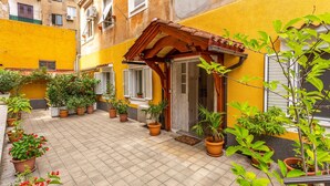 Een binnentuin met plantenpotten, een houten pergola en een geel gevelpand.