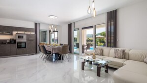 Een moderne woonkamer met een glazen salontafel, een beige bank en een eethoek met een tafel voor vier personen.