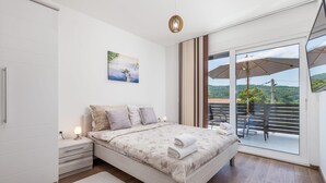 Een slaapkamer met een bed, nachtkastje, schilderij en uitzicht op het buitenland door een schuifdeur.
