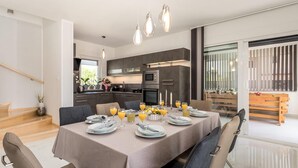 Een moderne eetruimte met een tafel voor zes personen, een keuken op de achtergrond en een balkon met een houten bank.