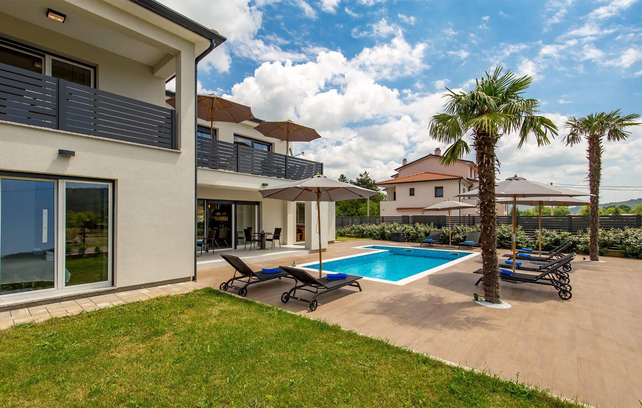 Een modern huis met een zwembad, terras en palmbomen.