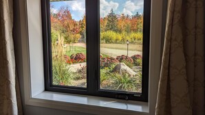 Una ventana con vista a un jardín con follaje otoñal y un cielo despejado.