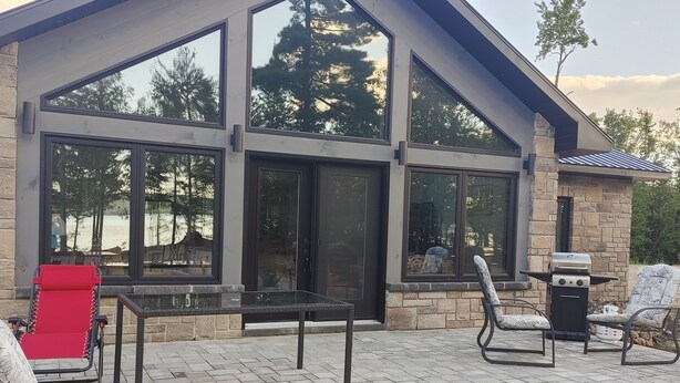 Una casa moderna con amplios ventanales, fachada de piedra y mobiliario exterior con mesa y sillas de vidrio.