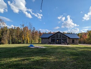 Eine Lodge mit Steinaußenwand und Metalldach, umgeben von einer Wiese und Bäumen mit Herbstlaub.