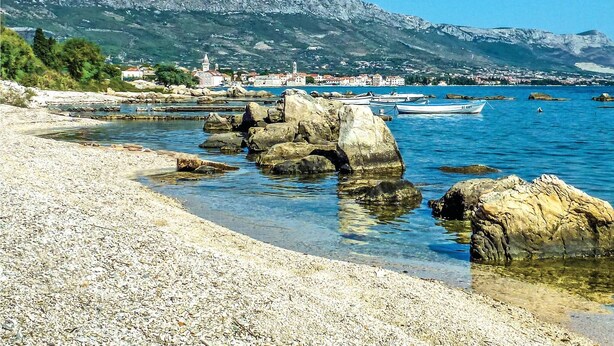 A pebble beach with clear water, boats, and a town in the background with mountains. - Lovely home in Kastel Stafilic (Kastel Stafilic)