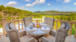 A dining table set for four with wicker chairs, a pool in the background, and a scenic view of hills and trees. - Stunning home in Pedreguer (Pedreguer)