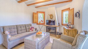 A cozy living room with a sofa, wicker chairs, a glass coffee table, a fireplace, and wooden beams on the ceiling. - Stunning home in Pedreguer (Pedreguer)