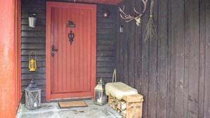 A wooden door with a red frame, a metal bucket, a lantern, a bench, and antlers on the wall.