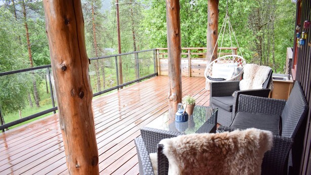 A wooden deck with wicker furniture, a hanging chair, and a glass table.