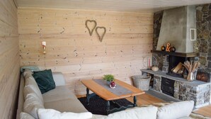A cozy living room with a stone fireplace, wooden walls, and a sofa with a green pillow.