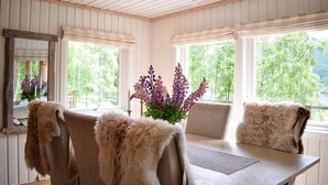 A room with a wooden table, four chairs with fur throws, a vase with purple flowers, and a mirror on the wall.