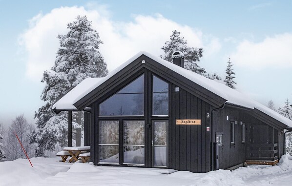 En træhytte med en stor glasdør og vinduer, mærket "Sagasthna", omgivet af sneklædte træer.