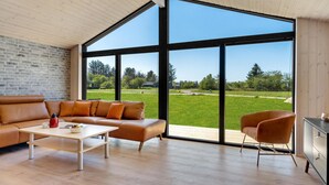 A modern living room with a large window, a leather sofa, a coffee table, and a chair. - Beautiful home in Hjørring with sauna (Hjørring)