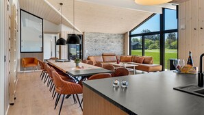 A modern kitchen with a large island, wooden cabinetry, and a stone backsplash. - Beautiful home in Hjørring with sauna (Hjørring)