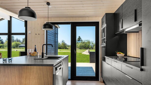 A modern kitchen with a large island, black appliances, and a view of a garden through the door. - Beautiful home in Hjørring with sauna (Hjørring)