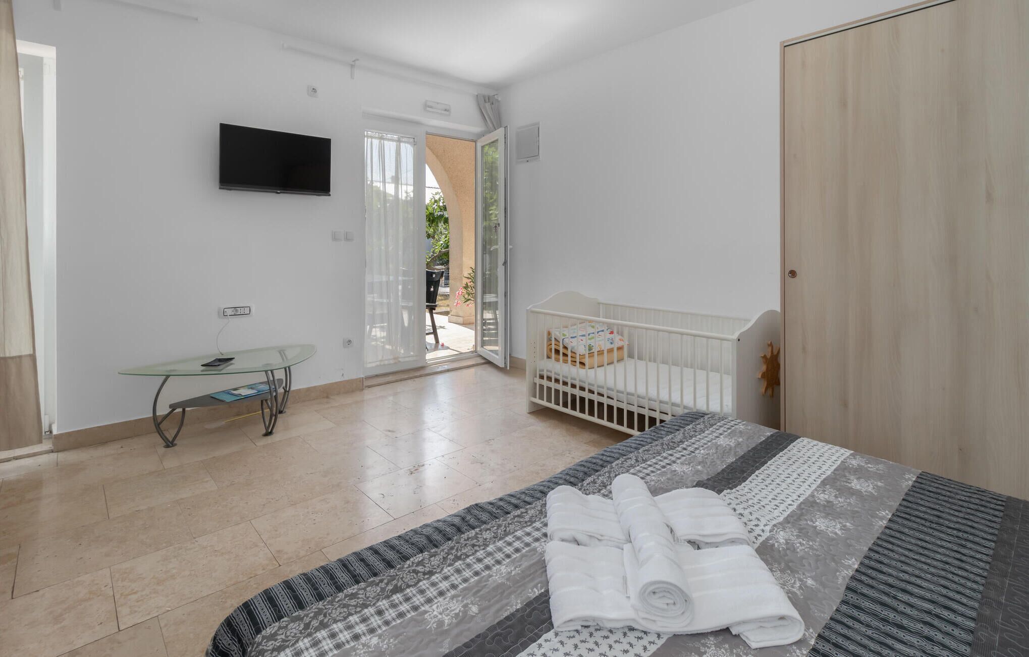 Quarto com cama, berço, mesa de vidro e televisão na parede.