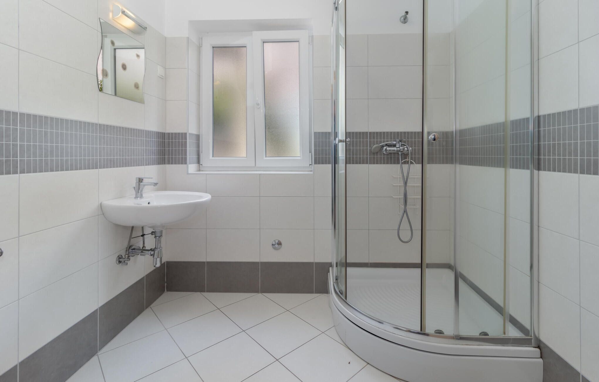 Un bagno moderno con doccia vetrata, un lavandino e una finestra sopra lo specchio.