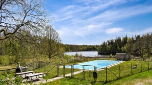 Ein Schwimmbecken, umgeben von einem eingezäunten Bereich mit Picknicktischen und einem Grill.