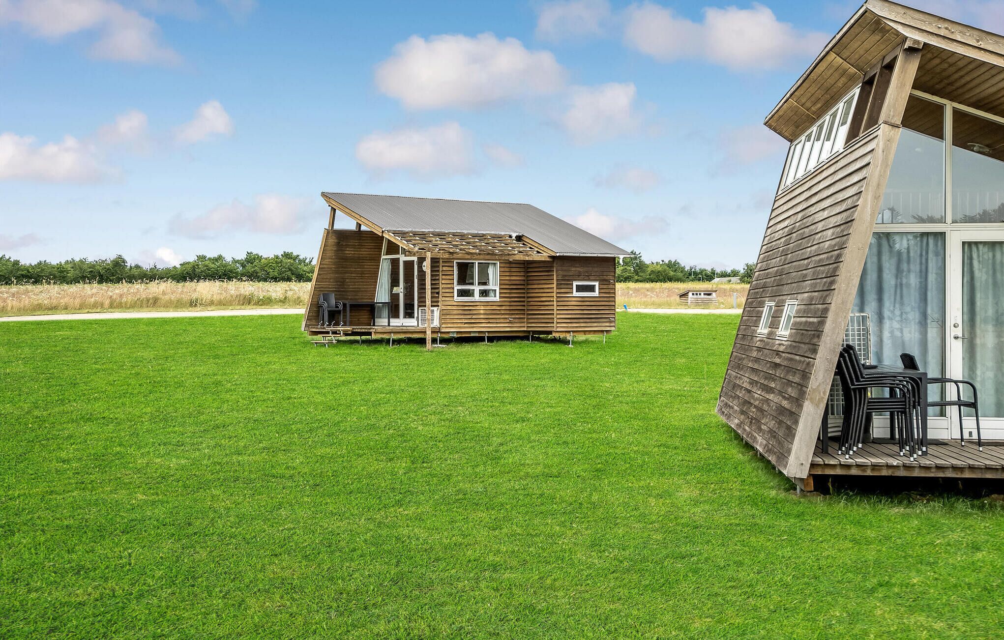 A wooden cabin with a sloped roof, a porch with chairs, and a large window.