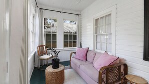 A cozy room with a white wooden ceiling, a pink sofa with matching cushions, wicker chairs, and a small round table with a potted plant. - Historic Bungalow Between Beach & Downtown (St. Augustine)