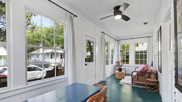 A covered porch with a dining table and chairs, a ceiling fan, and large windows overlooking a street. - Historic Bungalow Between Beach & Downtown (St. Augustine)
