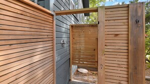A wooden outdoor toilet area with a metal door, a small round seat, and a brick pathway. - Historic Bungalow Between Beach & Downtown (St. Augustine)