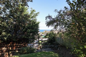 A garden with a wooden fence, a stone wall, and a view of the sea. - The Cottage at The Pines, Bull Bay. (Anglesey)