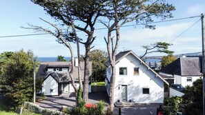 A coastal residential area with white houses, a stone wall, and a view of the sea. - The Cottage at The Pines, Bull Bay. (Anglesey)