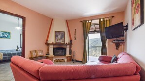 Una sala de estar con chimenea, un sofá, un televisor y un balcón con cortinas.