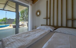A bedroom with two beds, a large window, and a view of a pool and outdoor furniture. - Luxurious home in Peroj (Peroj)