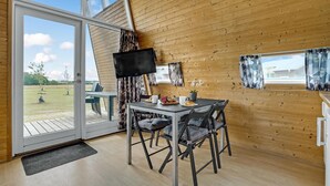 A cozy room with a wooden interior, a dining table with chairs, a flat-screen TV, and a view of the outdoors through large windows.
