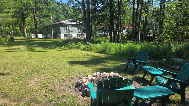 Un jardin avec un foyer, des fauteuils Adirondack verts et une maison en arrière-plan.