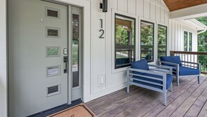 A porch with a gray door, a number '12' sign, and two blue chairs.