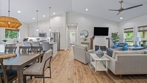 A modern open-plan living area with a dining table, sofas, and a kitchen in the background.