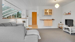 A modern living room with a grey sofa, a television, and a kitchen area with wooden cabinets and a hanging light fixture. - Stunning home in Fårvang with WiFi (Fårvang)