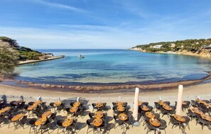 Vista costera con playa, muelle y zona de comedor con mesas y sillas.