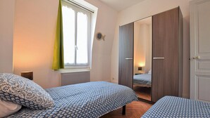 Une chambre avec deux lits, une fenêtre avec des rideaux, une armoire et un miroir.
