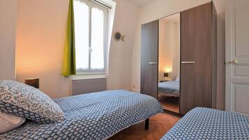 Une chambre avec deux lits, une fenêtre avec des rideaux, une armoire et un miroir.