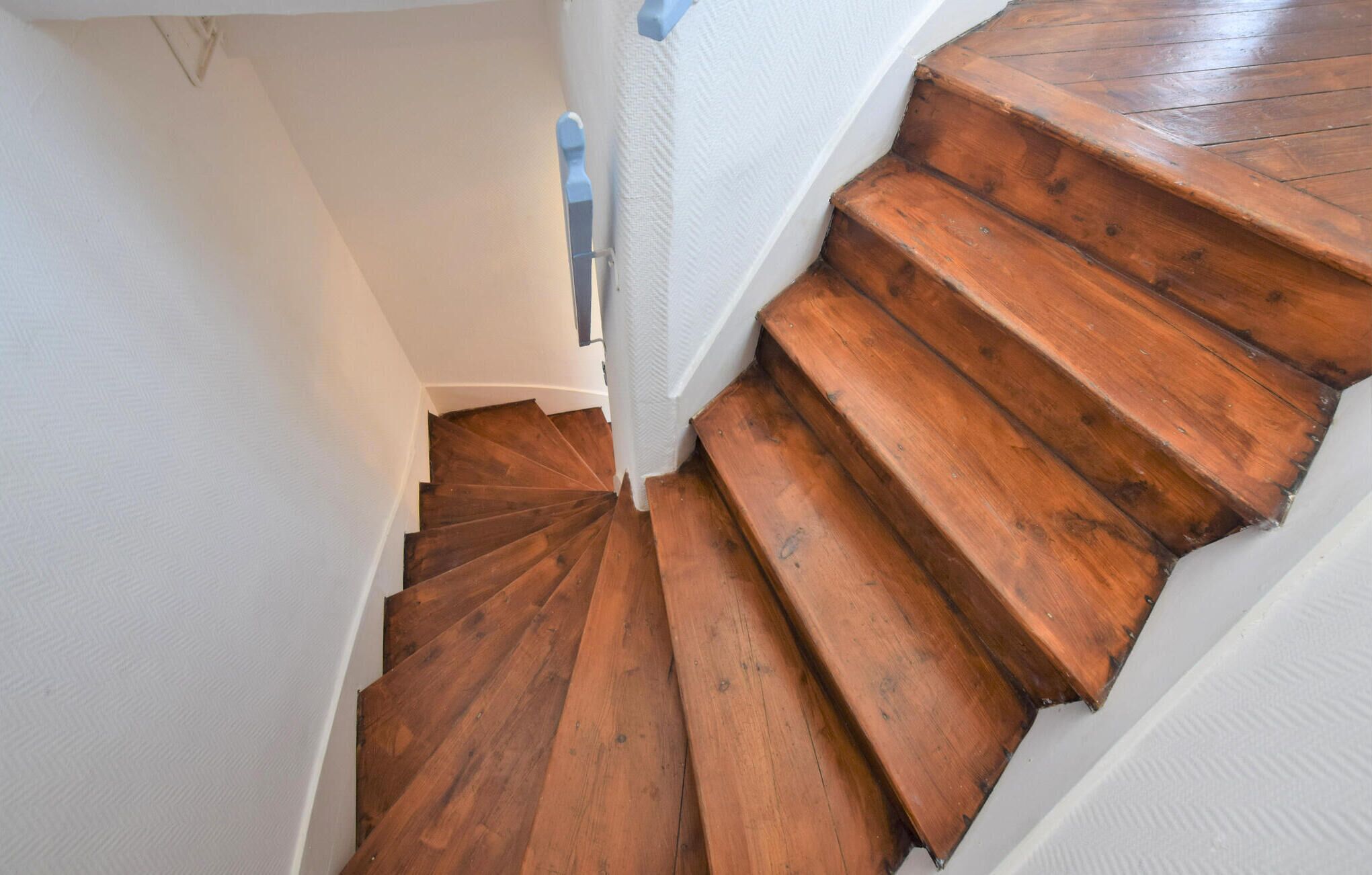 Eine Holztreppe mit weißen Wänden und einem blauen Geländer.